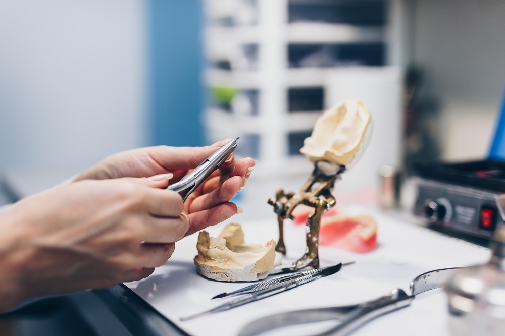 Dental prosthesis, female hands working on the denture. Selective focus.